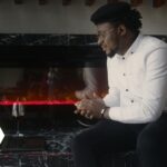 Casually dressed man using a laptop near a cozy fireplace indoors.